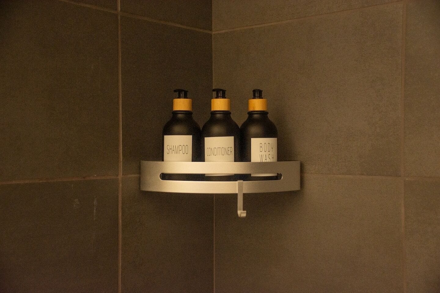 Baño con repisa que contiene tres botellas: champú, acondicionador y jabón de baño.
