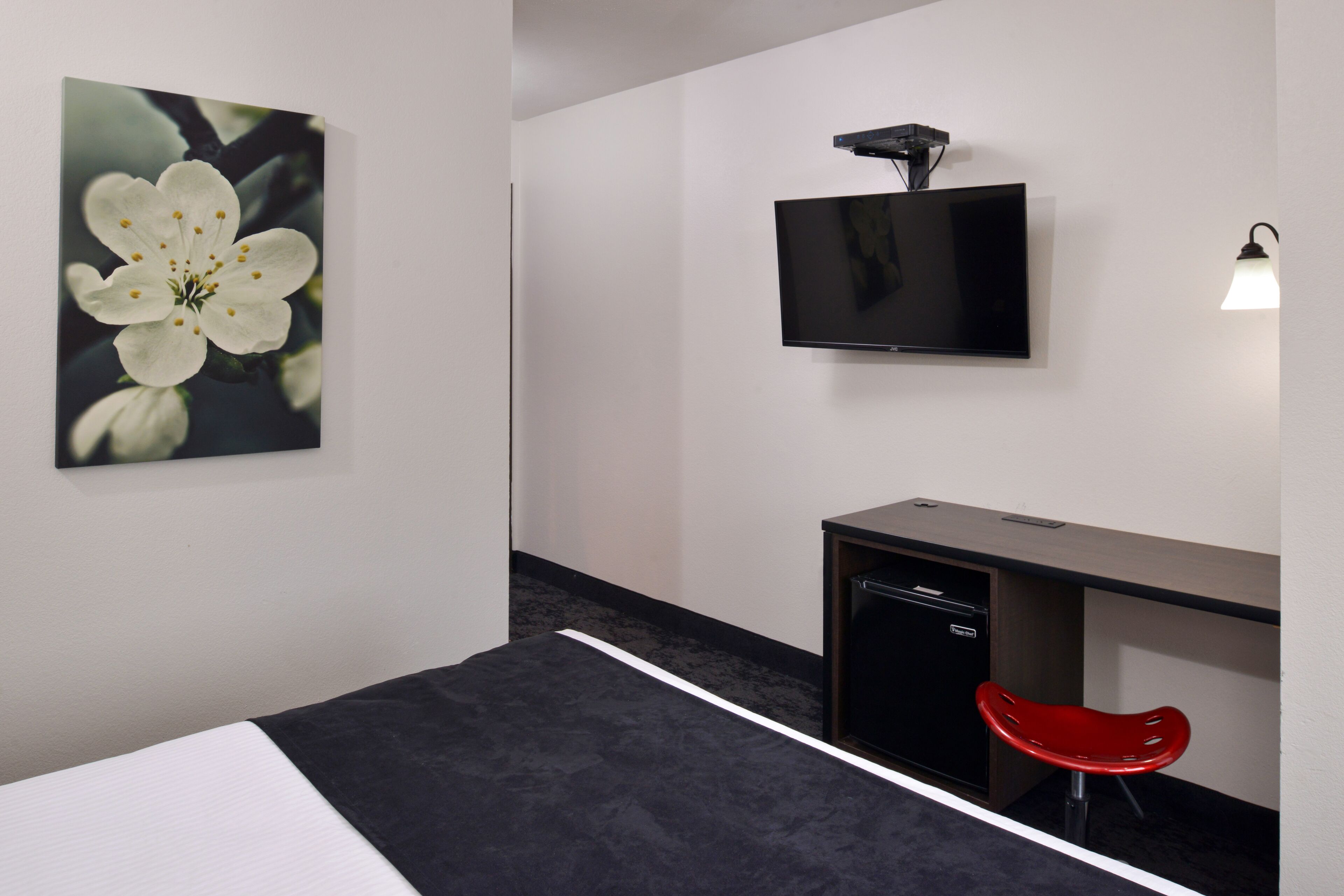 Ein Hotelzimmer mit Bett, Schreibtisch mit Stuhl, Fernseher und Wandleuchte.