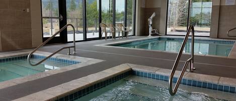 An indoor swimming pool with clear views of the outdoors, including trees and a distant mountain range.