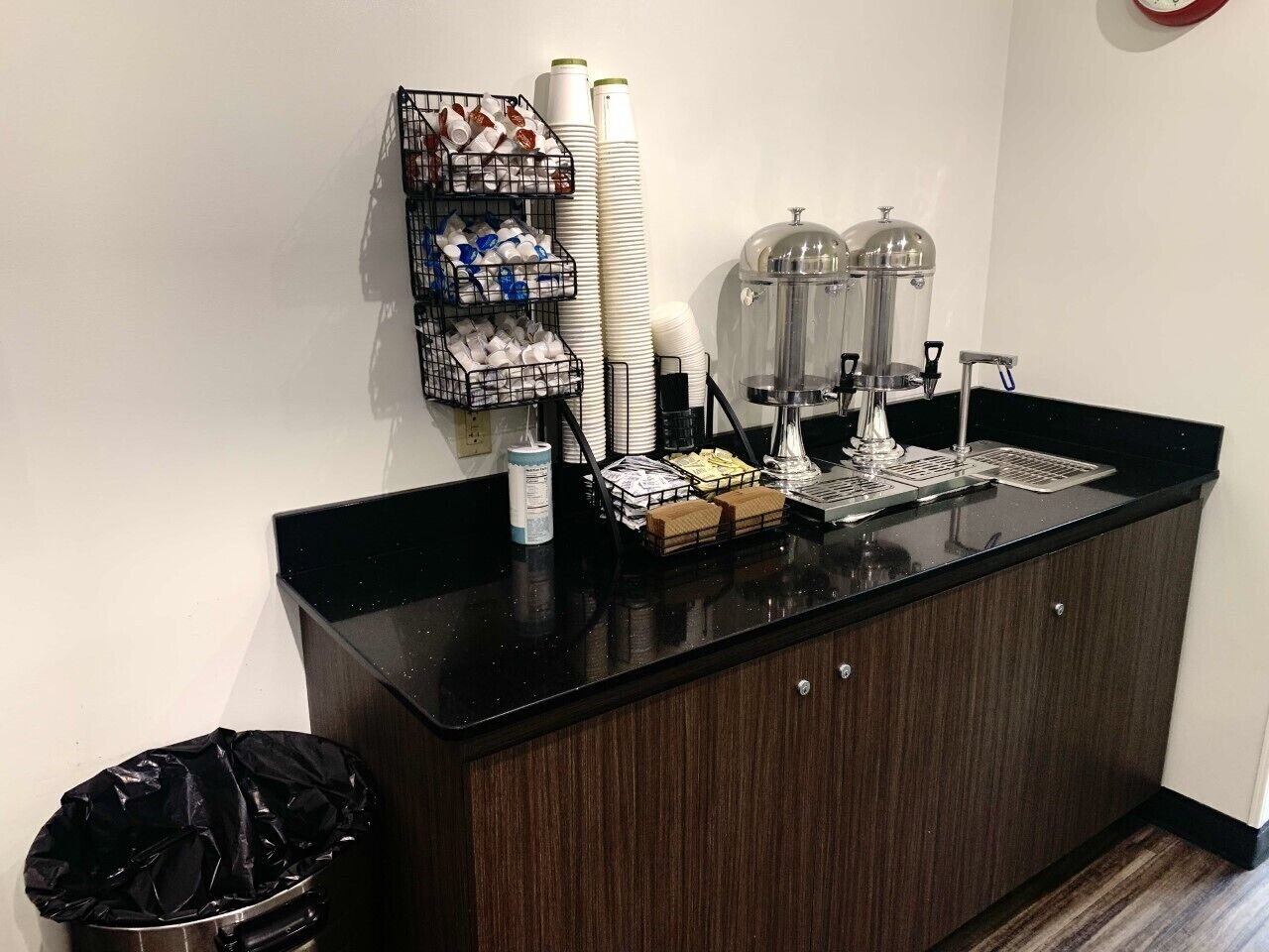 A counter with a coffee machine, a water dispenser, and a trash bin.