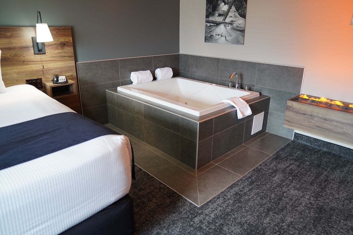 Une chambre d’hôtel moderne dotée d’un grand lit, d’une salle de bain séparée avec baignoire et d’une table de chevet avec une lampe.