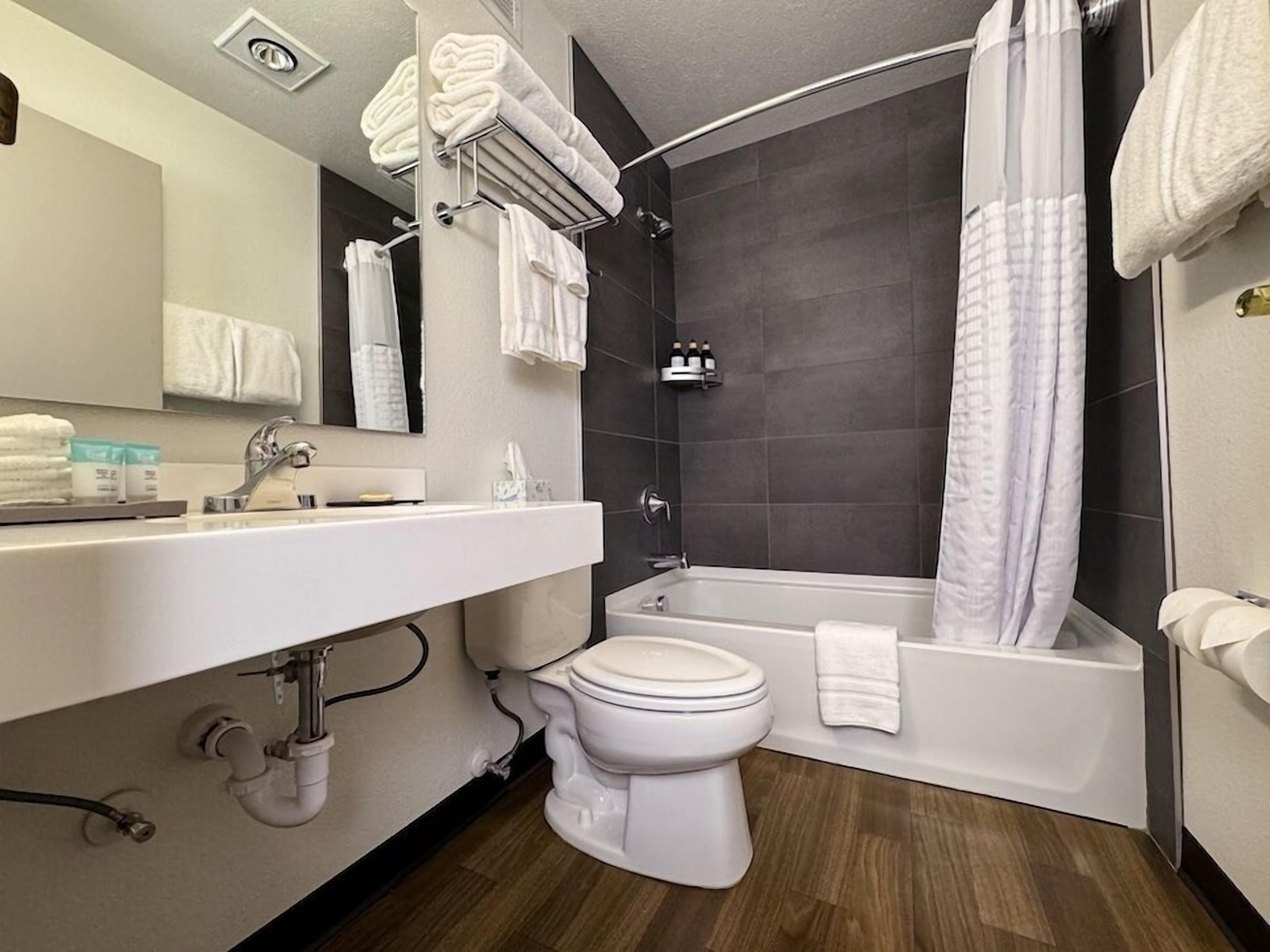 Un baño moderno con lavamanos, inodoro y bañera blancos. Hay toallas y artículos de aseo en la encimera.