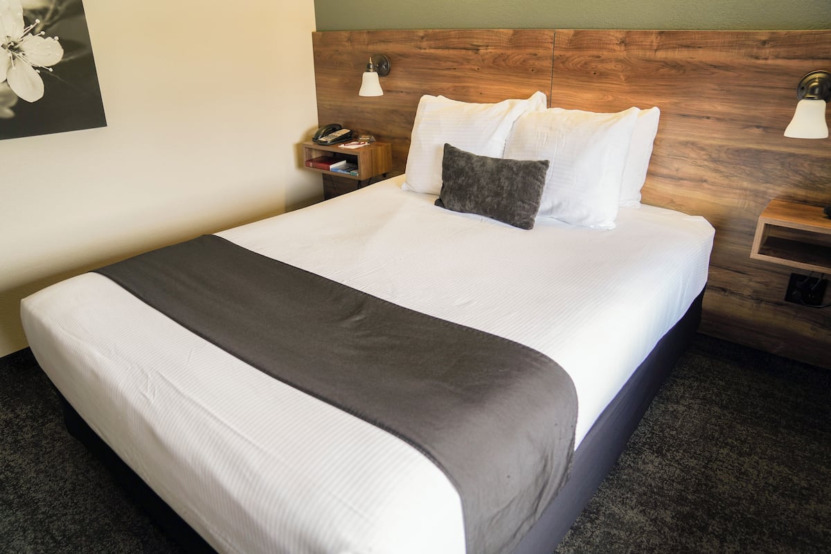 A neatly made bed with white and gray linens, a wooden headboard, bedside tables with lamps, and a framed picture on the wall.