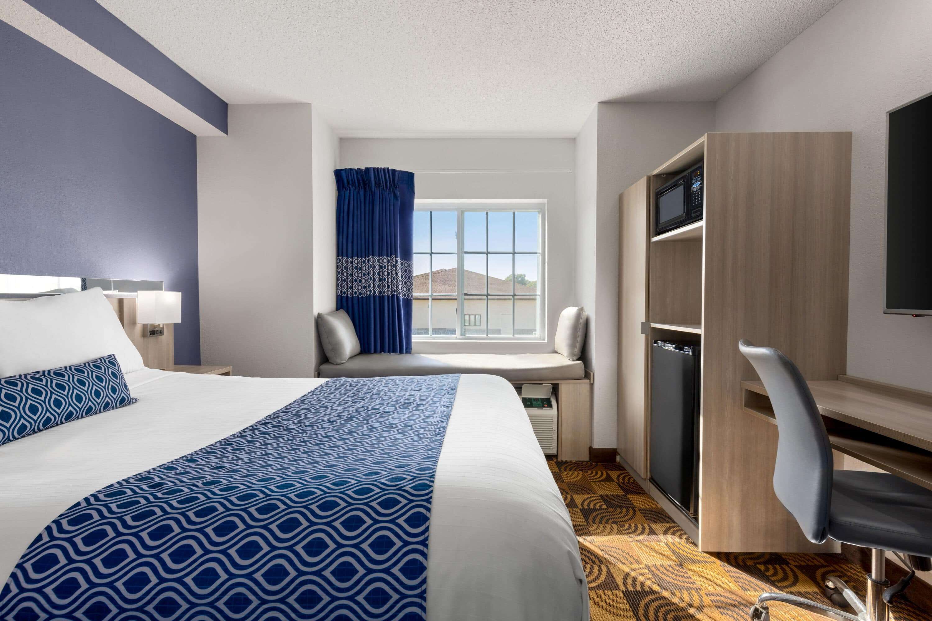 Habitación de hotel con cama, escritorio, silla, televisor y ventana con vistas al exterior.