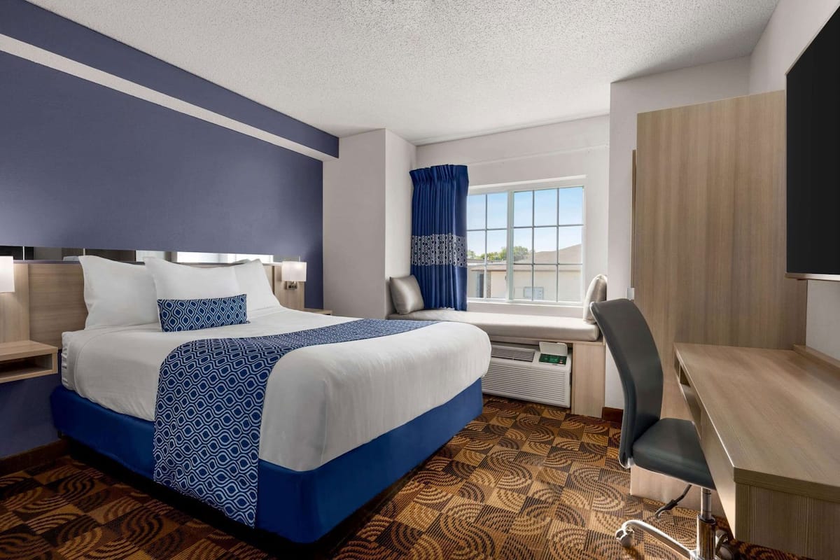 A hotel room with a bed, desk, chair, and a window with curtains.