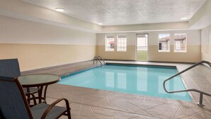 Une piscine intérieure avec une paroi en verre, une chaise et une table.