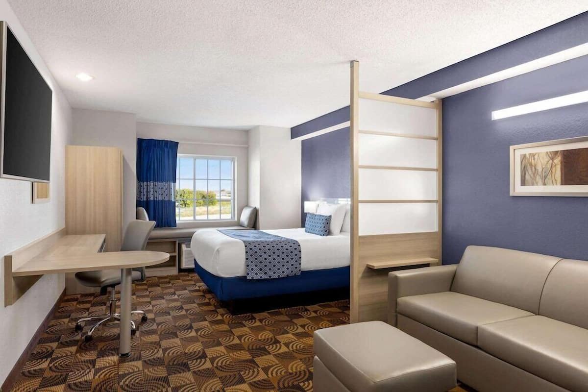 A hotel room with a bed, a desk, a chair, a sofa, and a patterned carpet.