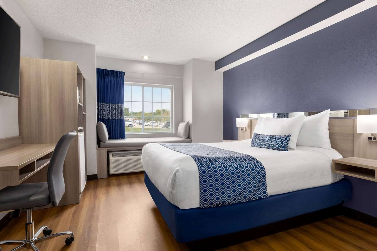 A hotel room with a bed, desk, chair, and a view of the outdoors.