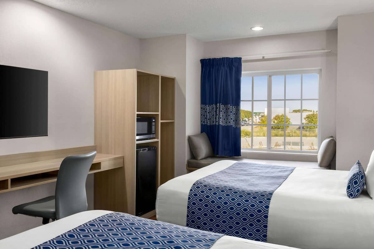 A hotel room with two beds, a desk with a computer, a wardrobe, and a window with a view of the outside.