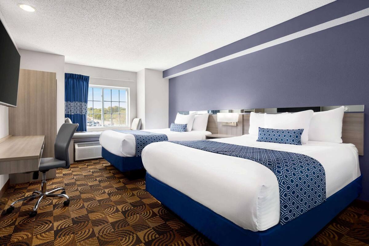 A hotel room with two beds, a desk, and a chair.