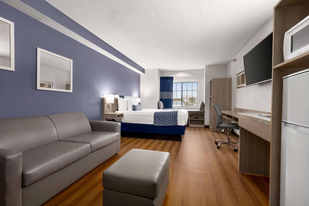 A modern hotel room with a bed, a sofa, a desk, and a TV.