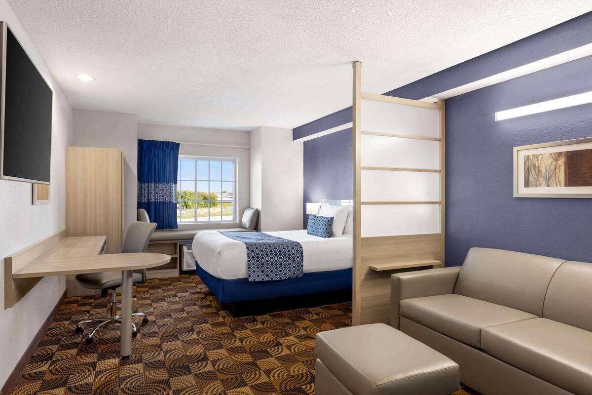 A hotel room with a bed, a desk, a sofa, and a window with curtains.