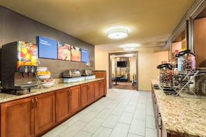 A hotel kitchen with a buffet setup, including a coffee station, fruit bowl, and a coffee machine.