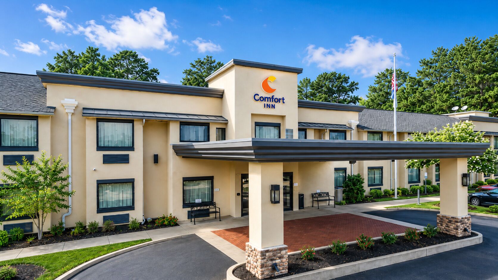 A Comfort Inn hotel with a covered entrance, a brick patio, and a landscaped area with small trees and shrubs.