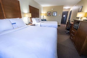 A hotel room with two beds, a desk, a chair, a microwave, and a door.