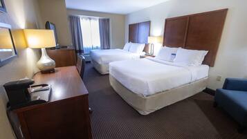 A hotel room with two beds, a desk with a lamp, a chair, and a window with curtains.