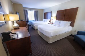 Une chambre d’hôtel avec deux lits, un bureau avec une lampe, une chaise et une fenêtre avec des rideaux.