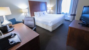 A hotel room with a bed, a desk with a computer, a chair, a TV, and a window with curtains.