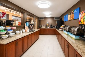 Et hotelmorgenmadsområde med et buffetbord, der indeholder forskellige spiser og drikkevarer.