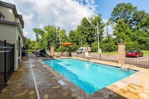 A swimming pool with a stone deck, a fence, and a red car in the background.