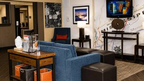 A hotel room with a sofa, armchair, table, lamp, TV, and a map on the wall. - Comfort Inn Tupelo Central (Tupelo)