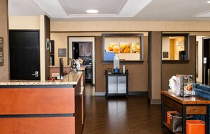 A hotel lobby with a reception desk, a small kitchenette, and a seating area with a coffee machine.