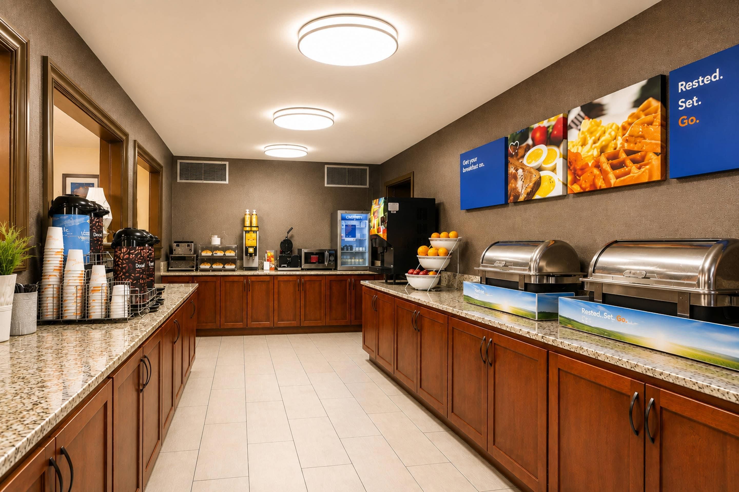 Een ontbijtruimte in een hotel met een buffet, waaronder een koffiehoek, een koelkast en een selectie ontbijtartikelen.