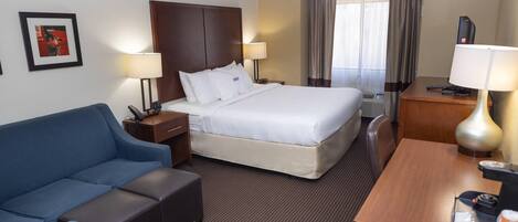 Una habitación de hotel con cama, escritorio, silla, sofá y mesita de noche.
