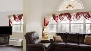 Una sala de estar con un sofá de cuero oscuro, un sillón de cuero, un televisor de pantalla plana y una mesita de noche con una lámpara.