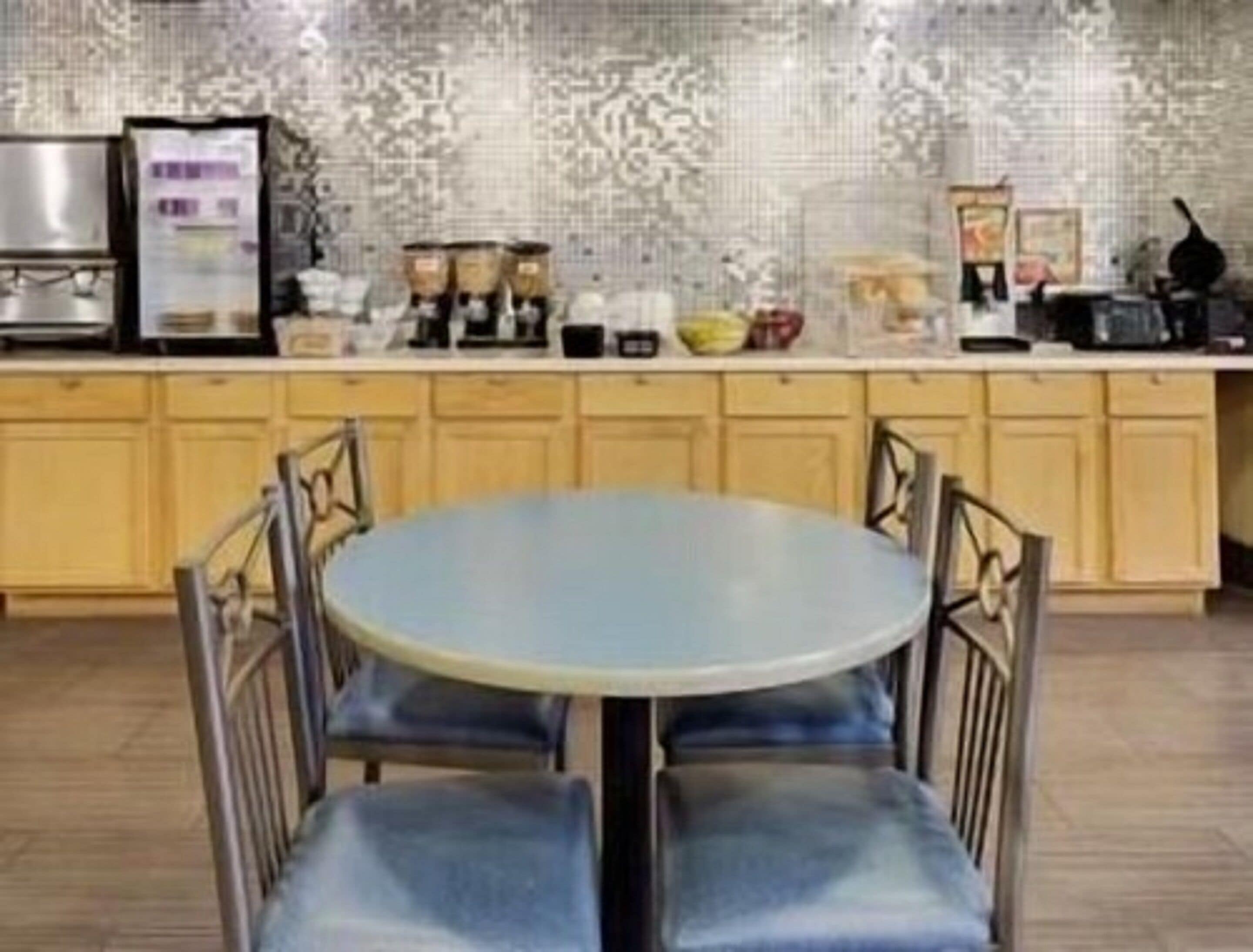 Una cocina con una mesa redonda y sillas, armarios de madera y diversos electrodomésticos.