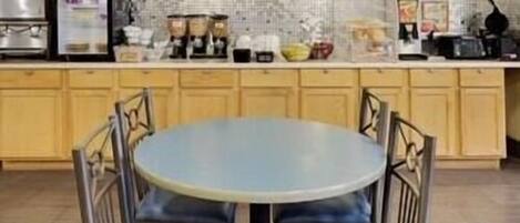 Una cocina con una mesa redonda y sillas, armarios de madera y diversos electrodomésticos.