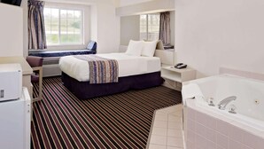 Habitación de hotel con cama, escritorio, silla, televisor, ventana con cortinas, baño con bañera y piso de baldosas.