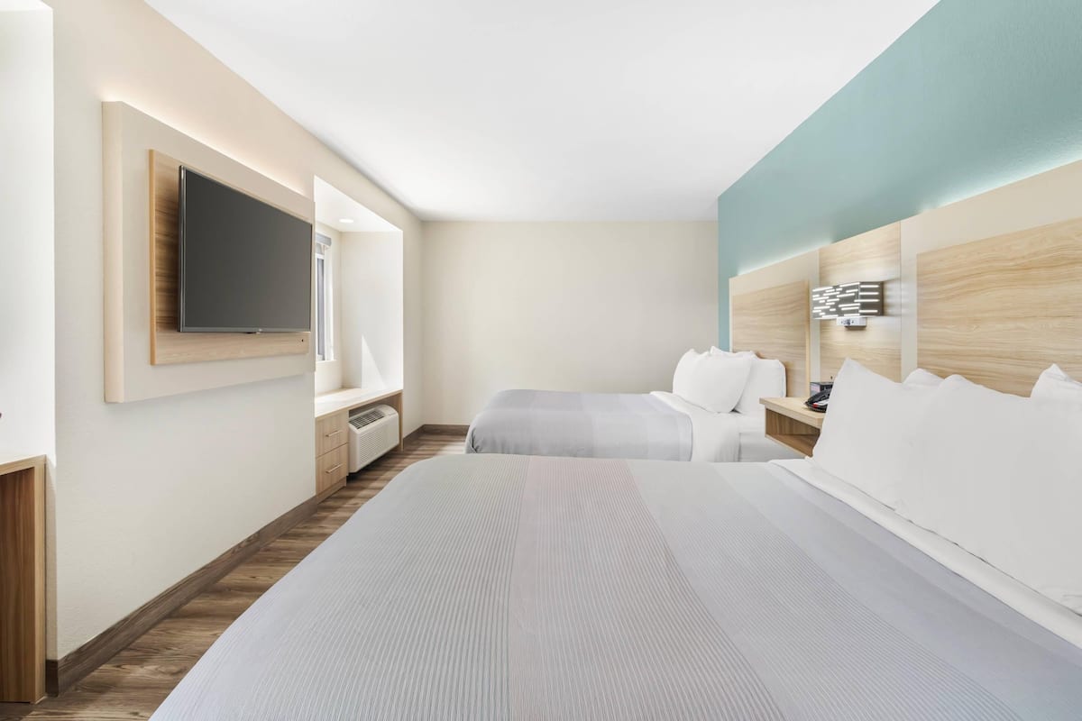 A hotel room with a large bed, a TV mounted on the wall, a bedside table, and a headboard with a light fixture.