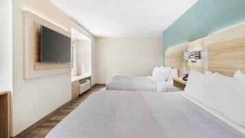 A hotel room with a large bed, a TV mounted on the wall, a bedside table, and a headboard with a light fixture.
