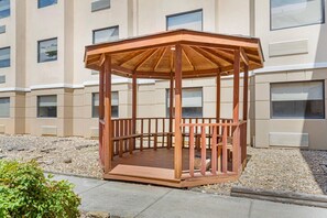 A wooden gazebo with a circular floor plan, surrounded by a gravel area and a building with multiple windows. - Quality Inn Knoxville West Cedar Bluff (Knoxville)