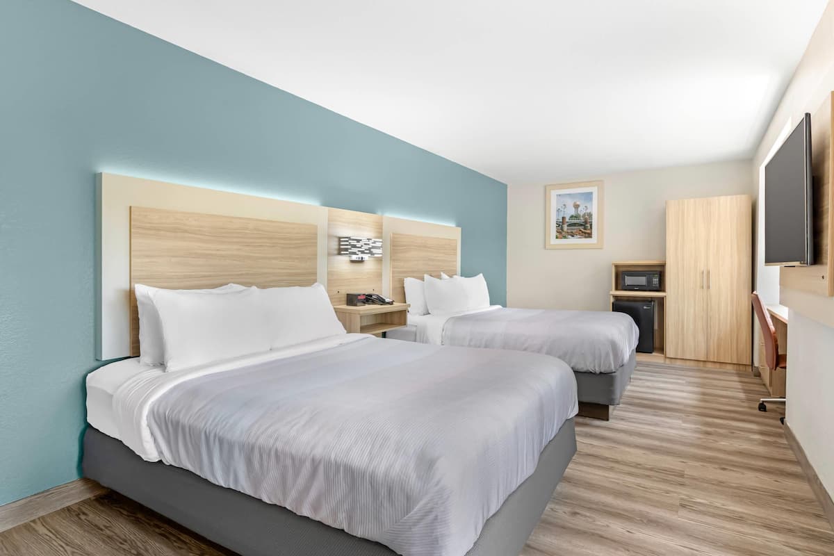 A hotel room with two beds, a desk, a TV, and a microwave.