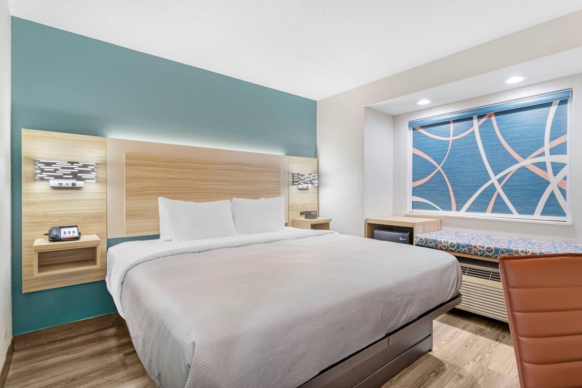 A modern hotel room with a large bed, bedside tables, a desk, and a window with a view.