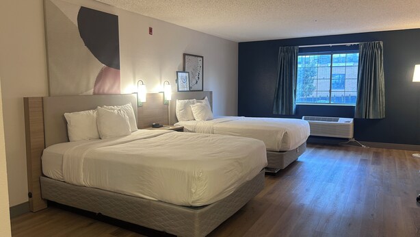 Habitación de hotel con dos camas, un ventanal con cortinas y un aire acondicionado de pared.