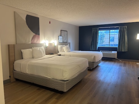 A hotel room with two beds, a large window with curtains, and a wall-mounted air conditioner.