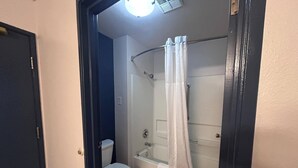 Un baño con inodoro, ducha con puerta de vidrio y cortina blanca.