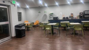 Un restaurante con mesas y sillas, un letrero de salida, un basurero y una máquina expendedora.