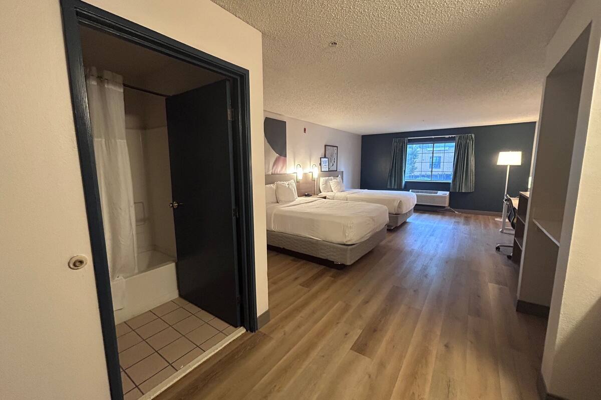 A hotel room with two beds, a window with curtains, a desk with a lamp, and a ceiling with a light fixture.