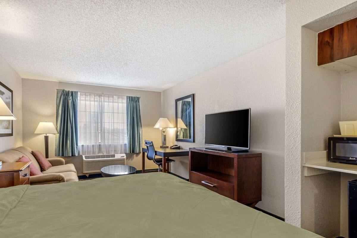 A hotel room with a bed, a desk, a chair, a television, and a window with curtains.