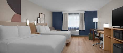 A hotel room with two beds, a desk, a television, and a window with curtains.