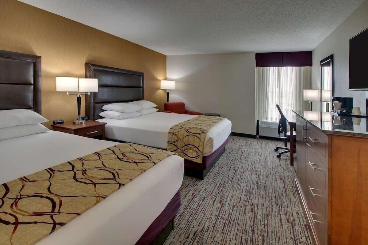 A hotel room with two beds, a desk, a chair, a TV, and a window with curtains.