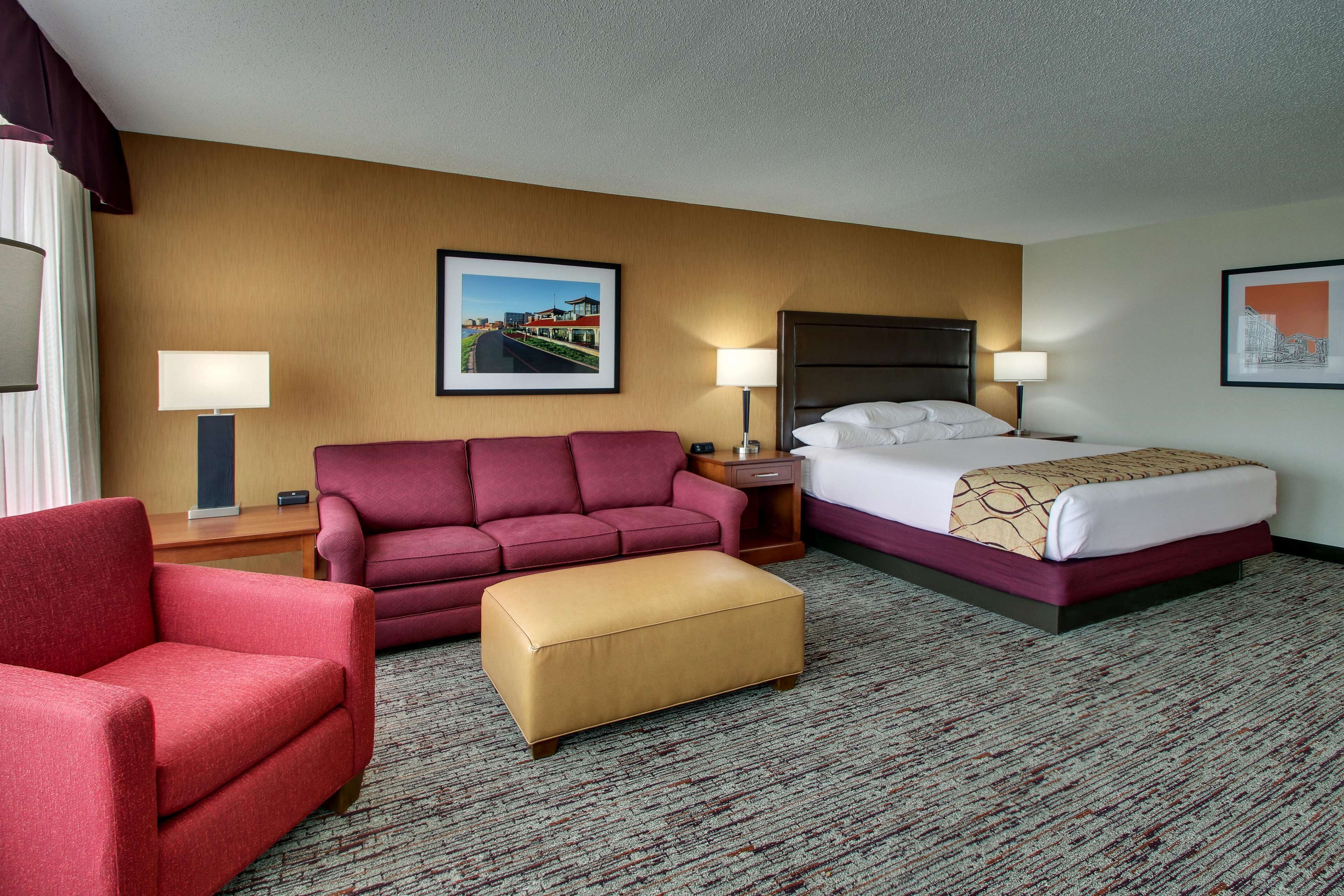 A hotel room with a bed, a red armchair, a sofa, and a small table.