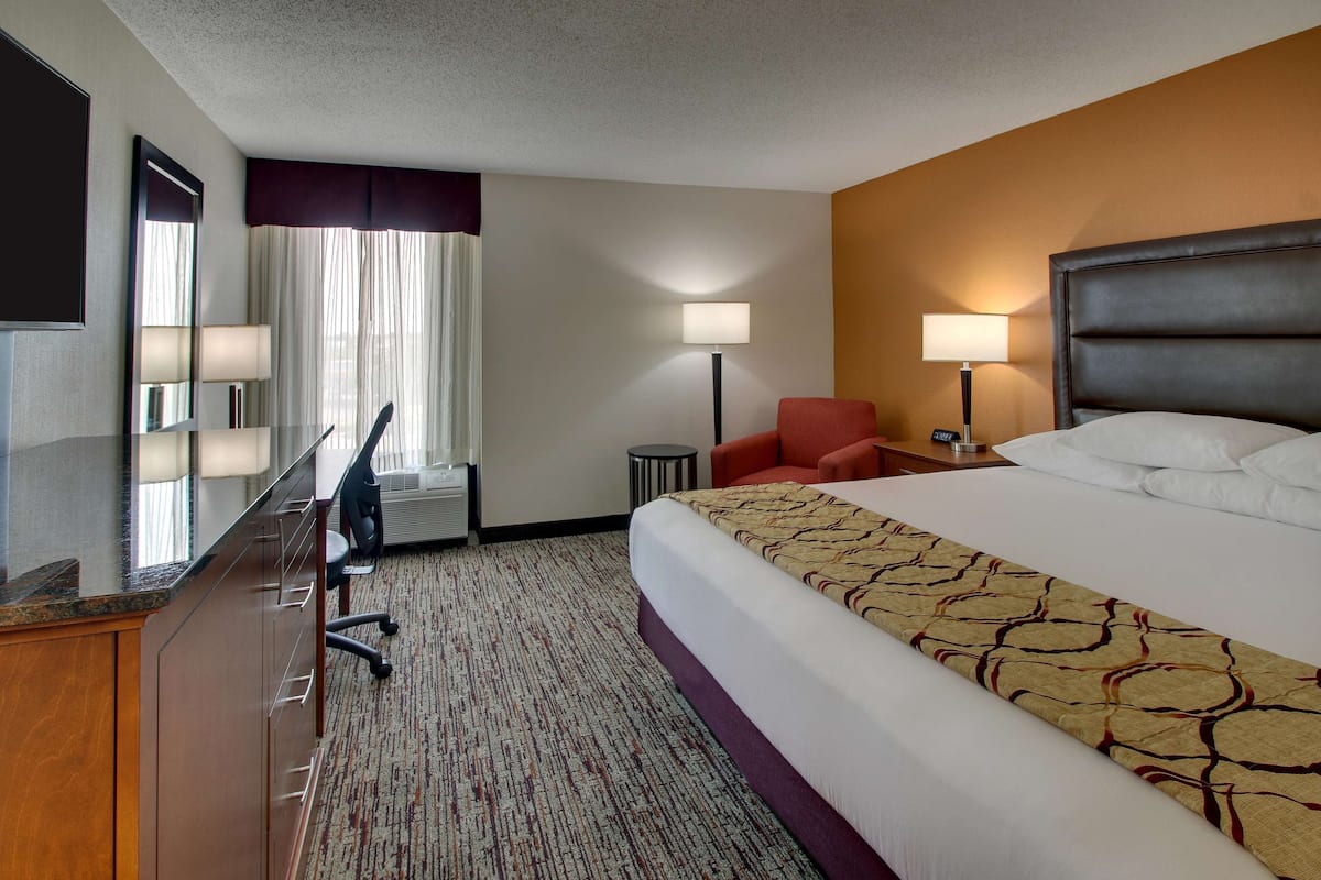 A hotel room with a bed, a desk, a chair, a TV, and a lamp.