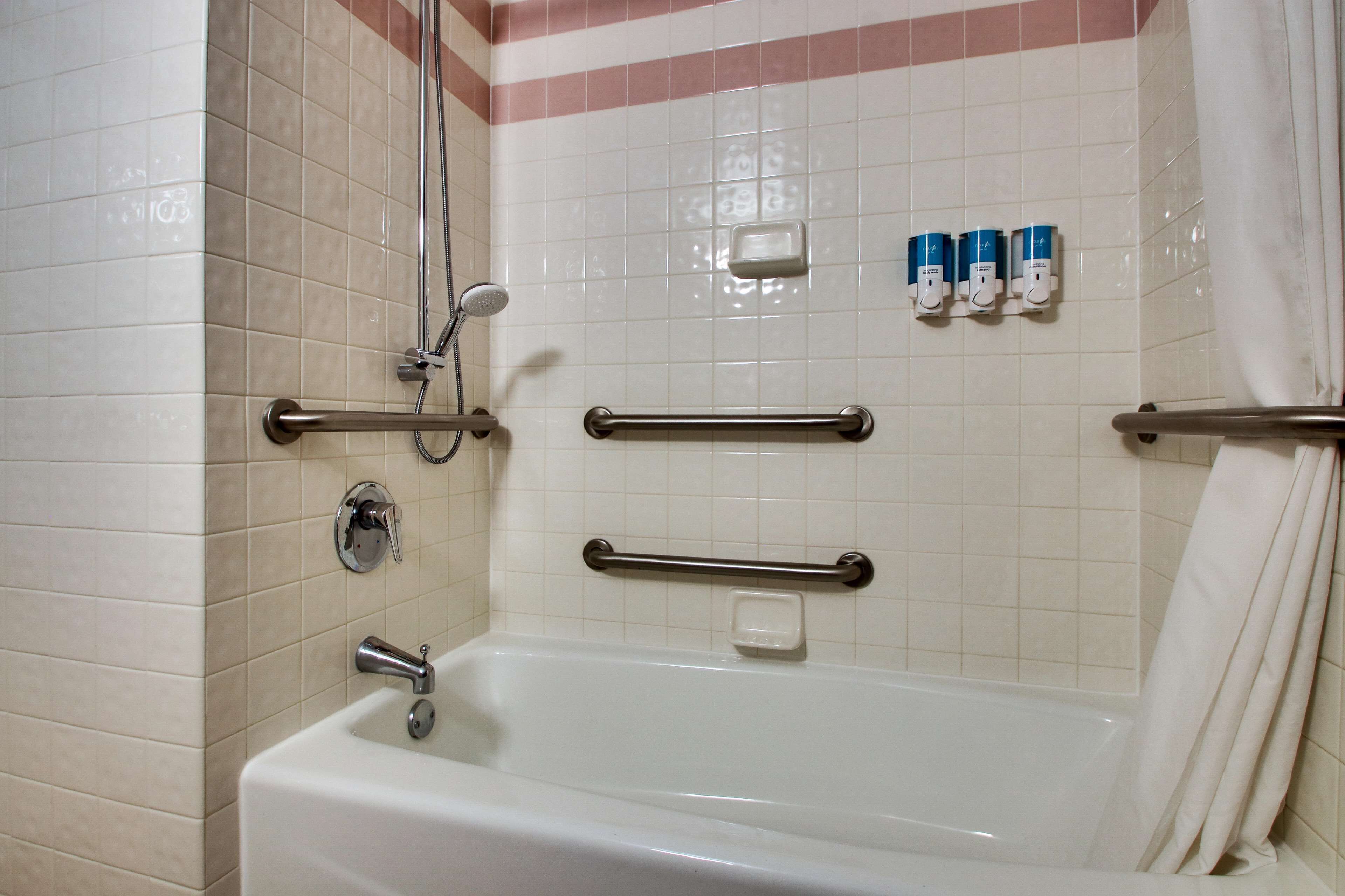 A bathroom with a bathtub, grab bars, a showerhead, and soap dispensers.