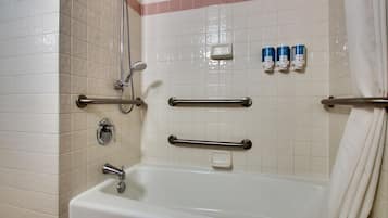 A bathroom with a bathtub, grab bars, a showerhead, and soap dispensers.
