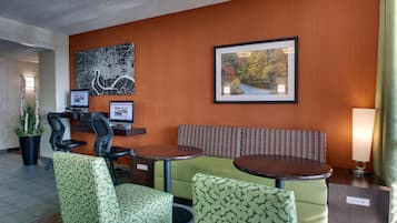 A hotel lobby with a reception desk, two computer monitors, a green sofa, a round table, and a framed picture on the wall.